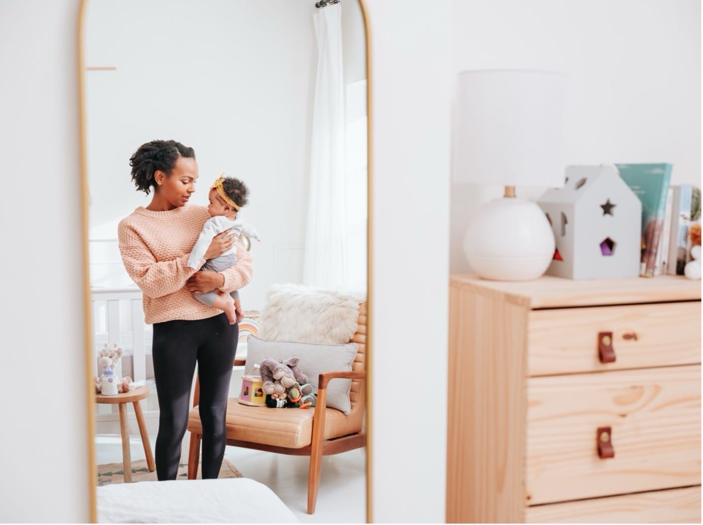 Reflection of a mom holding her baby in a long nursery mirror