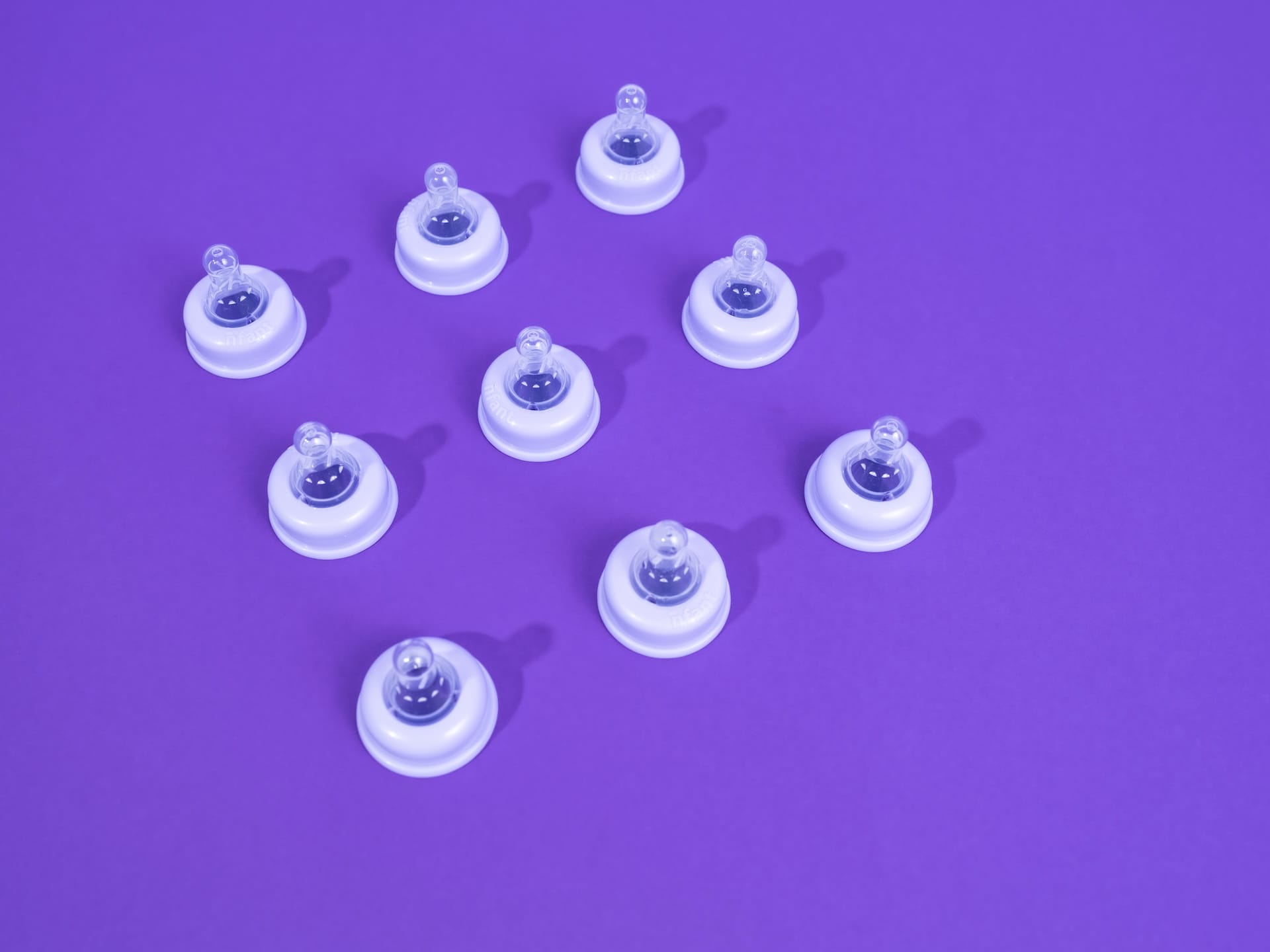 9 matching baby bottle nipples viewed from above on a purple background.