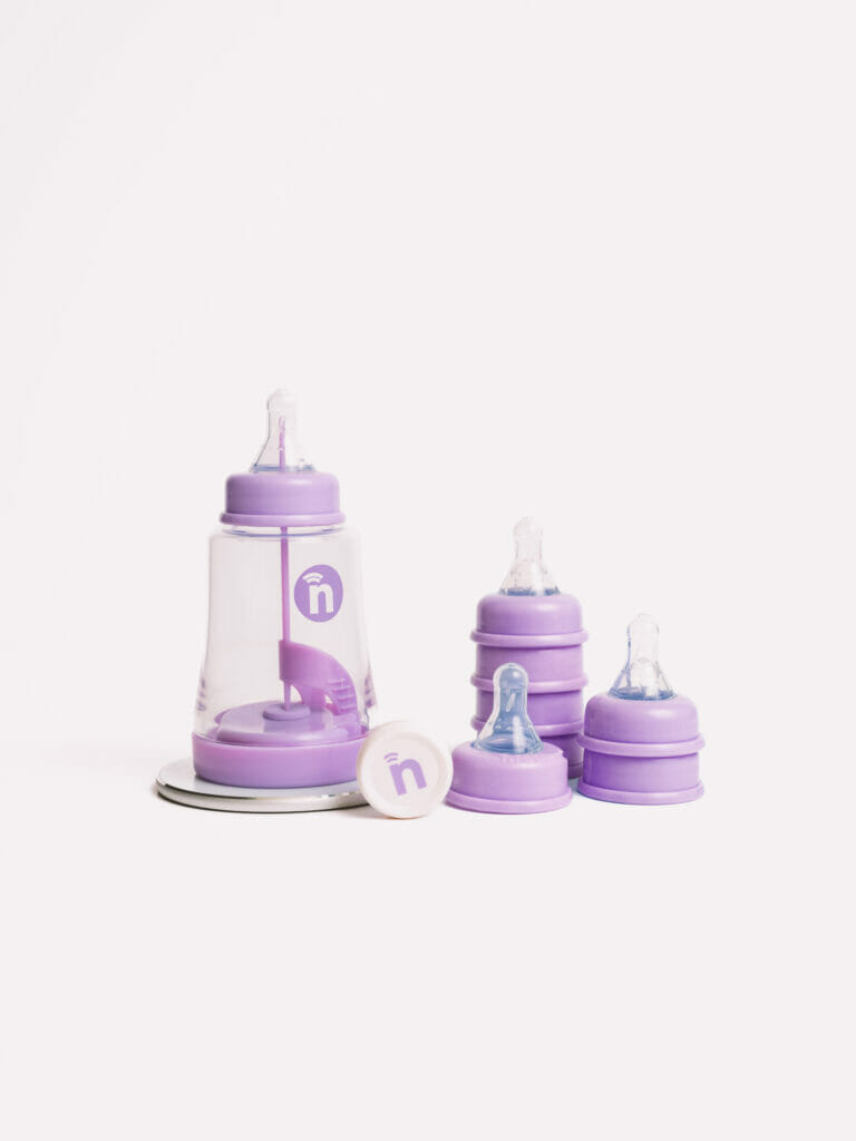 The full nfant® Thrive System is shown with the Smart Bottle, Smart Sensor, charging pad and an assortment of baby nipples.